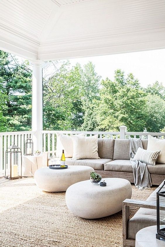 a large modern porch with neutral furniture, river stone ottomans, candle lanterns and neutral textiles