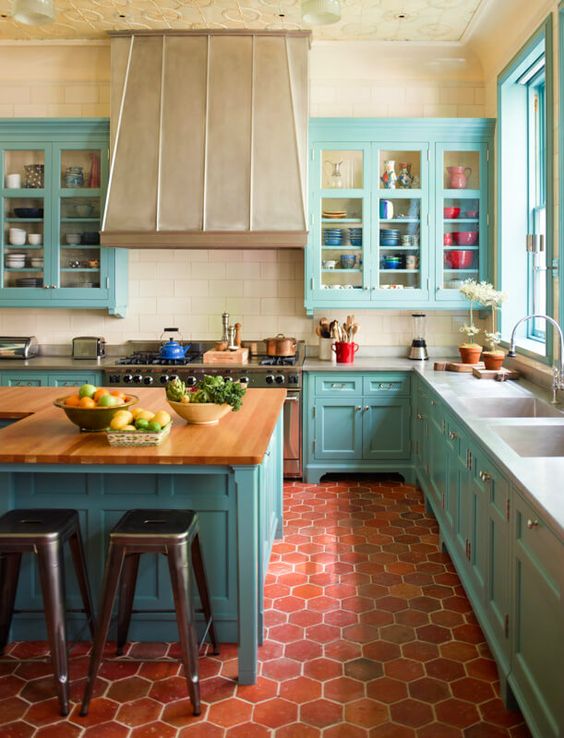a light blue kitchen in vintage style, with neutral countertops, a large hood and kitchen island plus metal stools
