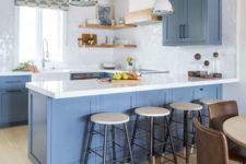 a light blue kitchen with white stone countertops and a white tile backsplash, open shelves and wooden beams is welcoming