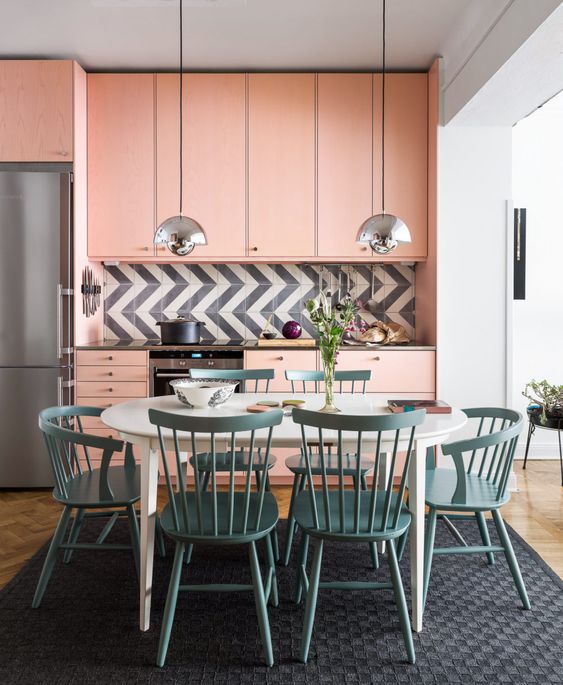 a light pink mid century modern kitchen with a graphic tile backsplash and a dining zone in blue right here