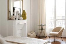 a lovely neutral Parisian bedorom with a faux fireplace, a statement mirror, a soft chair and a side table