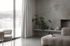 a minimalist living room with a concrete floor and wall, a grey sectional, a white chair and a glazed wall