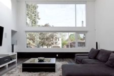 a minimalist living room with a large skylight and window, a TV unit, a dark sectional sofa and a coffee table