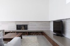 a minimalist living room with a long storage unit along several walls, a concrete floor, comfy furniture and touches of wood