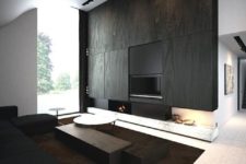 a minimalist space with a black wood clad wall with a built-in fireplace, dark coffee tables and a black sectional