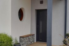a modern and laconic front door porch with a bench with rocks inside, greenery in pots and a stylish door