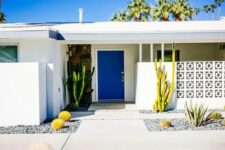 a modern desert entrance with a screen, a bold blue door, growing cacti and tiled pathways is a chic mid-century modern space