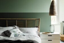 a modern green bedroom with a rattan bed, contrasting bedding, a white nightstand, a woven pendant lamp