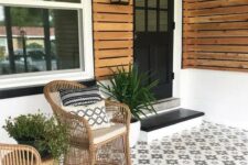 a modern porch clad with pretty star-patterned tiles, with rattan chairs, potted greenery and a black door and steps is a chic idea