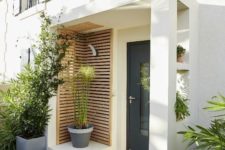 a modern porch with wooden slab screens, greenery in pots and mustard rubber boots