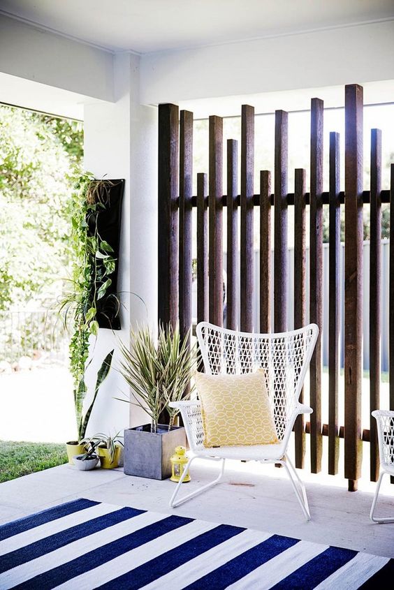 a modern private porch with a striped rug, a white woven chair, bright mustard touches and greenery