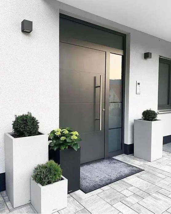 a modern to minimalist front porch with neutral and black square planters with greenery, a heavy black door and a rug