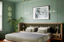 a monochromatic bedroom with a green ceiling and walls, a bed with an extended upholstered green headboard and catchy pendant lamps