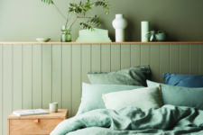 a monochromatic green bedroom with matte walls and beadboards, green bedding and touches of natural wood