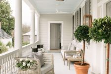 a neutral and welcoming summer porch with neutral wicker furniture, a wooden sofa, potted trees