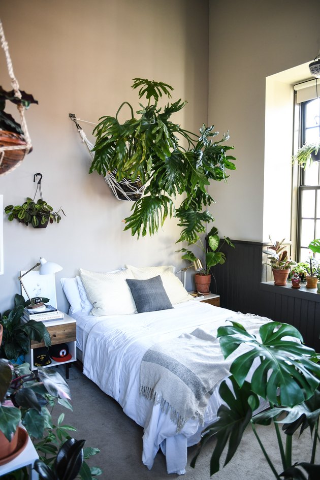 a neutral bedroom with wooden furniture and gold touches plus lots of tropical plants for a vibe