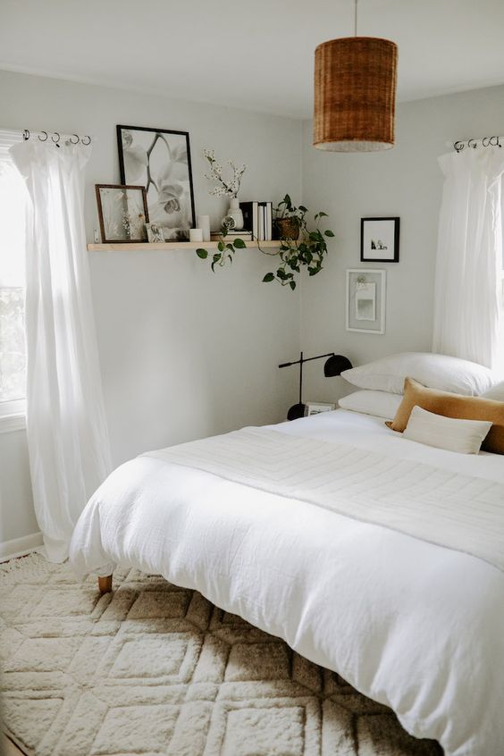 a neutral boho bedroom  wiht a wooden bed, nightstands, black lamps and a woven one, a shelf with books and greenery