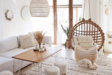 a neutral boho living room with white furniture, a suspended chair, a wooden table and stools