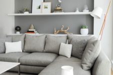 a neutral contemporary living room with a grey sectional, white floating shelves and a marble coffee table