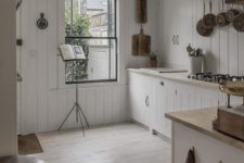 a neutral cottage kitchen with white beadboard, wooden countertops, railings, a large window with much natural light