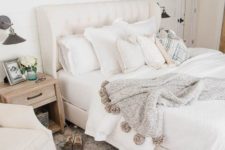 a neutral farmhouse bedorom with a creamy bed, wooden nightstands, neutral textiles, artworks on the wall and vintage sconces