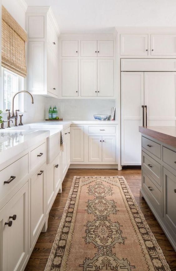 a neutral farmhouse kitchen with white marble tiles, woven shades, a boho rug and a grey kitchen island