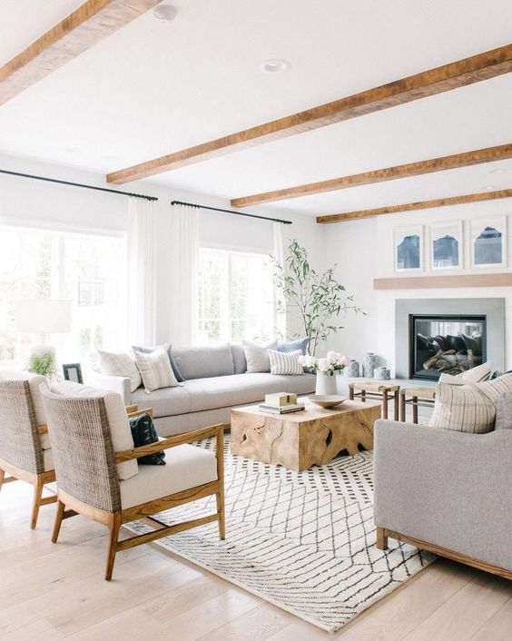 a neutral farmhouse living room with grey furniture, a wooden table, wooden beams, a built in fireplace and a gallery wall