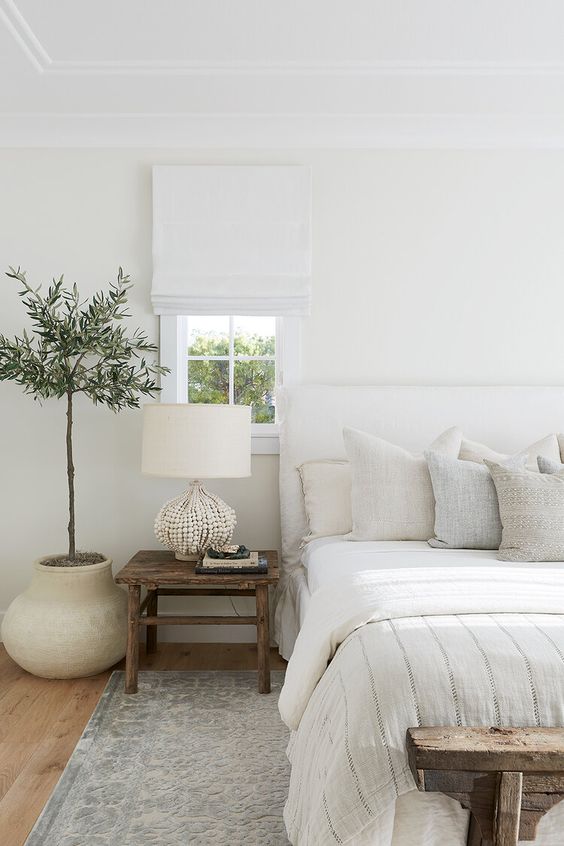 a peaceful natural bedroom with a white bed, a wooden bench and nightstands, a catchy beaded lamp and a statement plant