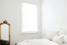 a pure white bedroom with a bed, nightstands and lamps, a wooden bench, a vintage mirror and a chic crystal chandelier