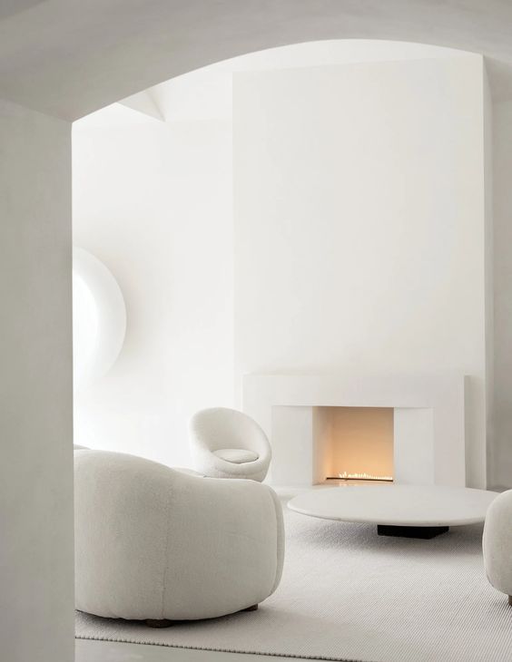 A pure white minimalist living room with a built in fireplace, white chairs and a table