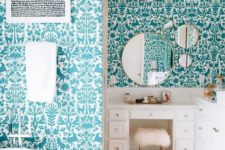 a quirky bathroom with walls covered with flora and fauna turquoise wallpaper, white furniture and appliances looks fun