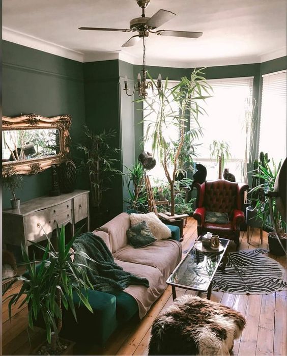 a quirky living room with hunter grene walls, a matching sofa, lots of potted greenery and touches of animal prints