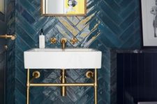 a refined bathroom with blue herringbone clad tiles, a chic sink on a stand, sconces and brass touches