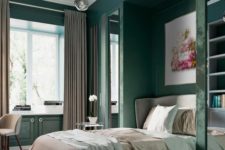 a refined bedroom with dark green walls and storage units, grey and green textiles, a bright artwork and a chandelier