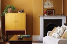 a refined living room with warm yellow walls, a mustard cabinet, a crystal chandelier and exquisite furniture and a fireplace