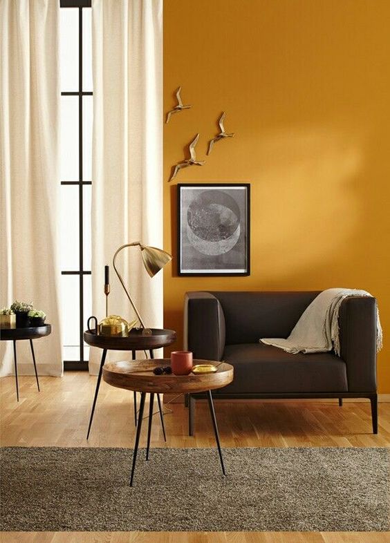 a refined living room with warm yellow walls, chic furniture, artworks on the wall and white curtains