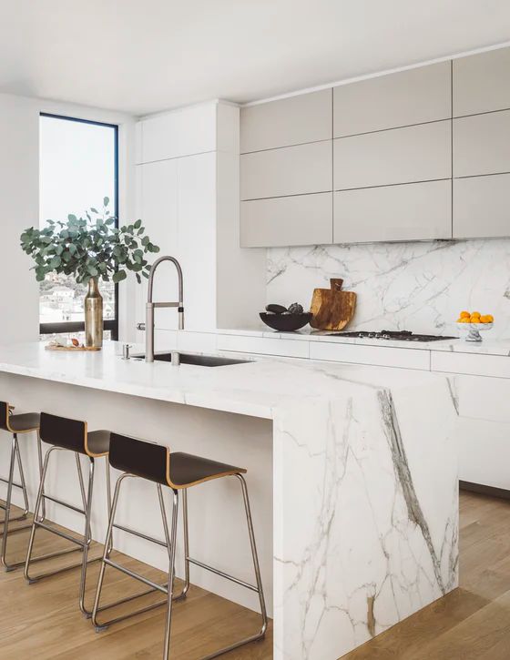 a refined minimalist kitchen with sleek cabinets, tan uppers, a white marble backsplash and countertops, black stools