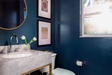 a refined navy powder room with a marble vanity, a crystal chandelier, gold touches and a neutral tile floor