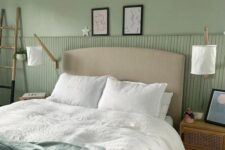 a sage green bedroom with a greige upholstered bed, neutral bedding, cane nightstands, lamps and some art