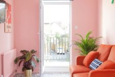 a small bright living room with pink walls, an orange sofa, a gallery wall and potted plants for more glam