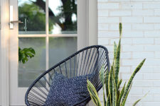 a small modern porch with a black woven chair, a printed pillow and a statement plant in a pink pot