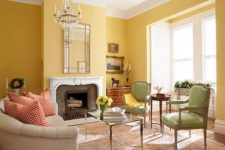 a sophisticated living room with yellow walls, green chairs, a vintage fireplace and a crystal chandelier