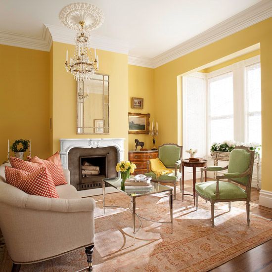 a sophisticated living room with yellow walls, green chairs, a vintage fireplace and a crystal chandelier