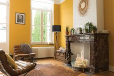 a stylish living room with sunny yellow walls, a non-working fireplace with candles and leather furniture