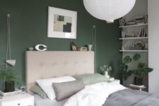 a stylish modern bedroom with a hunter green accent wall, neutral furniture and some potted greenery