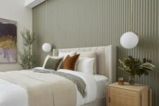 a stylish modern bedroom with a sage green fluted accent wall, a neutral upholstered bed with neutral bedding, rattan nightstands and pendant lamps