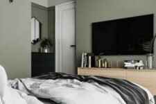 a stylish modern bedroom with sage green walls, an upholstered grey bed with grey bedding, a stained dresser and a black one
