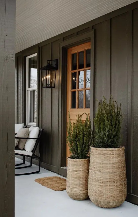 a stylish modern front porch with black trim walls, woven planters with greenery, a woven rug, a white upholstered chair