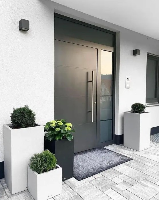 a stylish modern porch with a black metal door, grey and black tall square planters with greenery