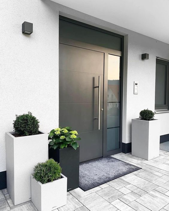 a stylish modern porch with a blakc metal door, grey and black tall square planters with greenery